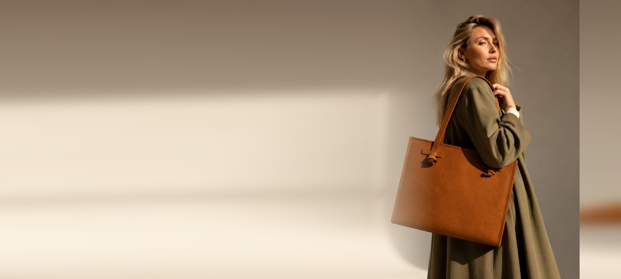 A woman in a long coat carrying a cognac full-grain leather tote bag over her shoulder.
